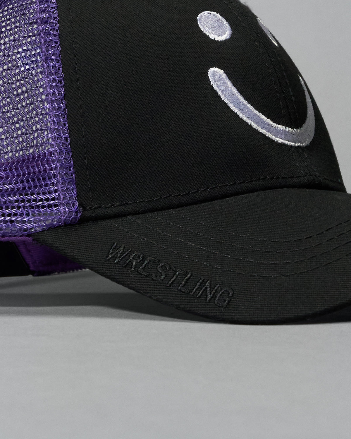 Black and purple cap with smiley face design on a gray background