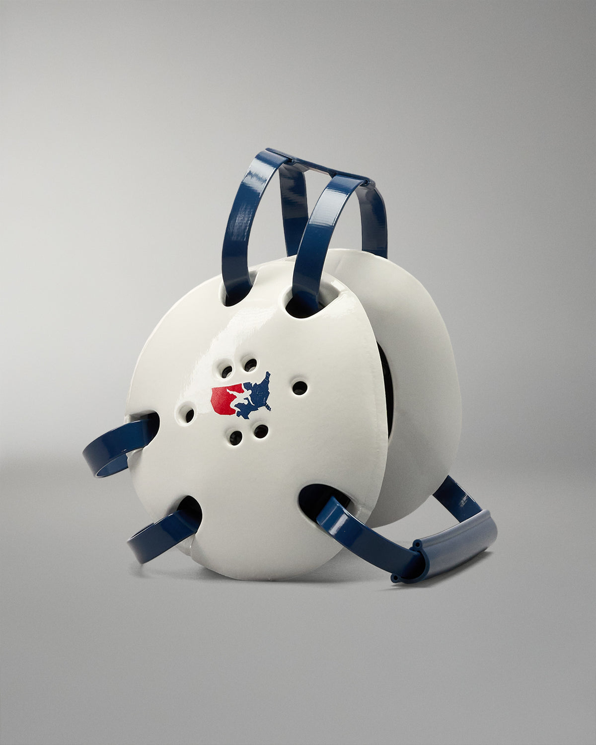 White protective wrestling headgear with blue straps on a gradient blue background. USA Wrestling logo on the headgear side
