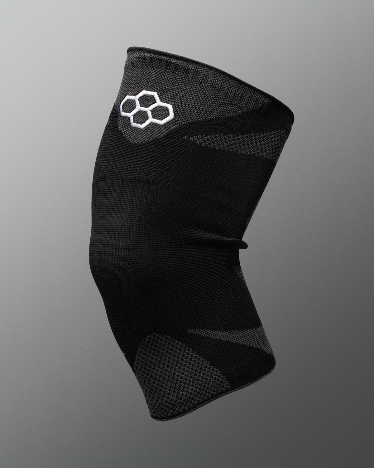A black athletic knee sleeve with a white Quadhex logo on the upper section, displayed against a neutral gray gradient background.