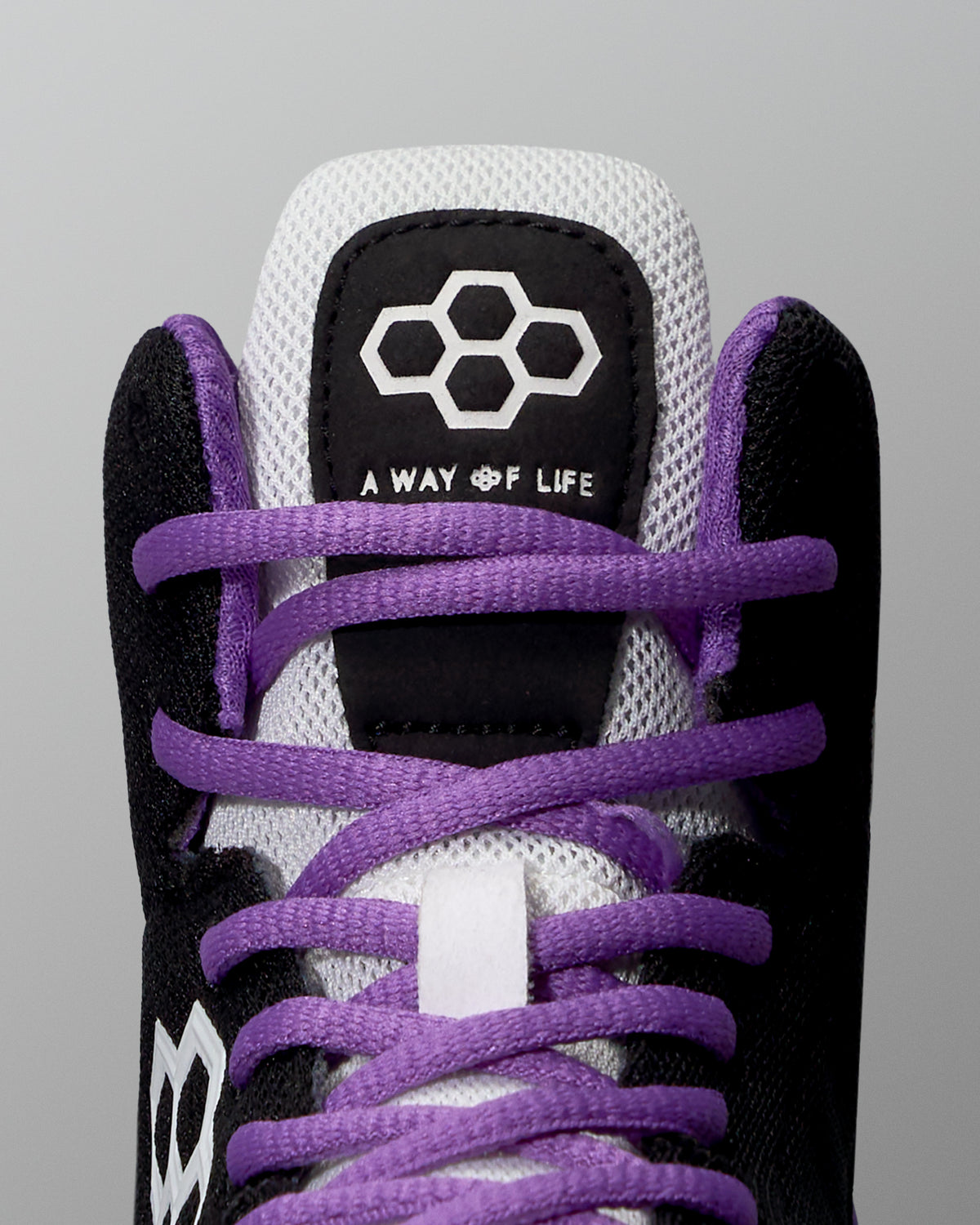Close-up of a sneaker with purple laces and black and white accents on a gray background.