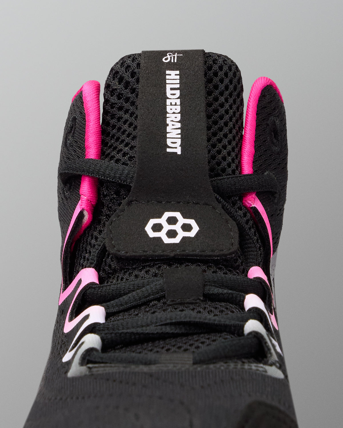 Close-up of the top of a black wrestling shoe with bright pink accents and white branding details, including the text 'HIDERBRANDT' on the tongue pull tab.