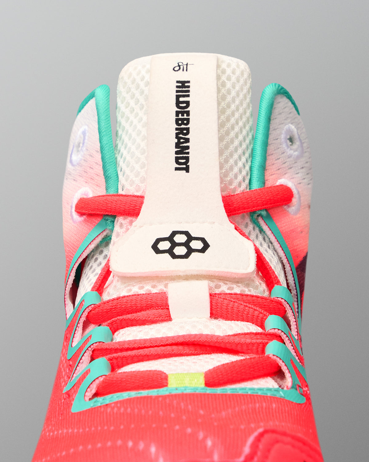 Close-up of the RUDIS Hildebrandt 2.0 Girls Wrestling Shoe tongue featuring Hildebrandt branding, RUDIS logo, coral laces, and teal supports.