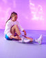 Person sitting on a floor wearing a white sweatshirt, blue shorts, and white sneakers with green accents.