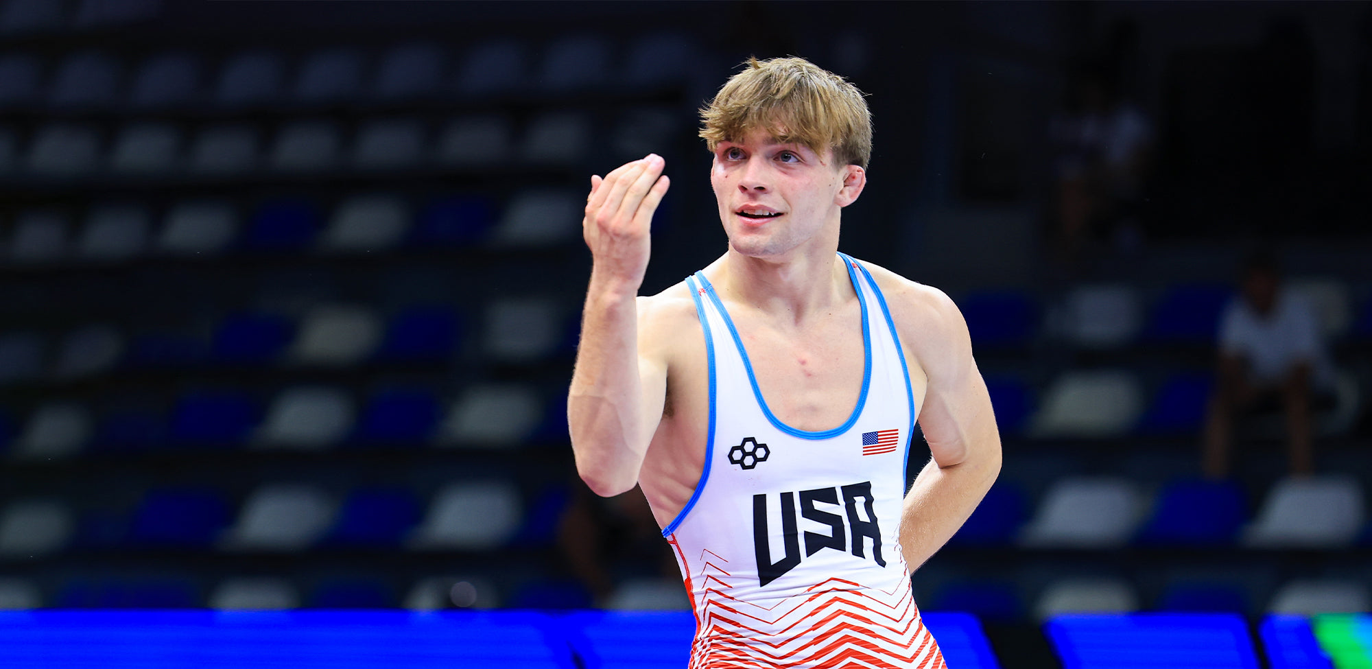 Marcus Blaze in a USA Wrestling singlet during competition, gesturing confidently after a match — representing Team USA and RUDIS on the international wrestling stage.
