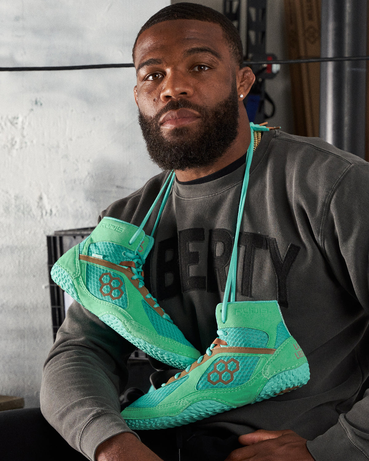 A man wearing a dark sweatshirt with LIBERTY text poses with vibrant green athletic shoes hanging around his neck showcasing their unique design and colors