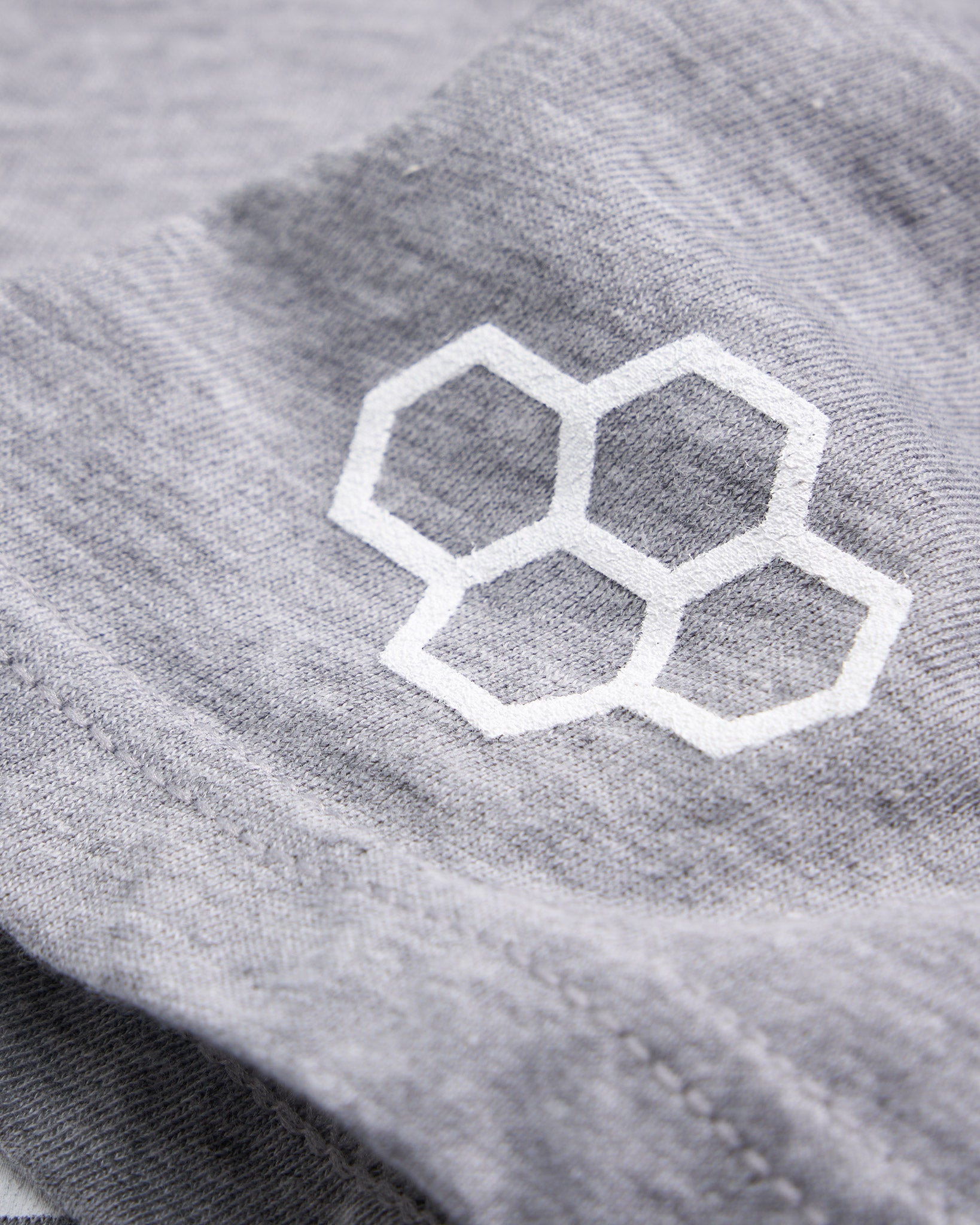 A close-up view of a light gray fabric featuring a white hexagonal logo highlighting the texture and detail of the material