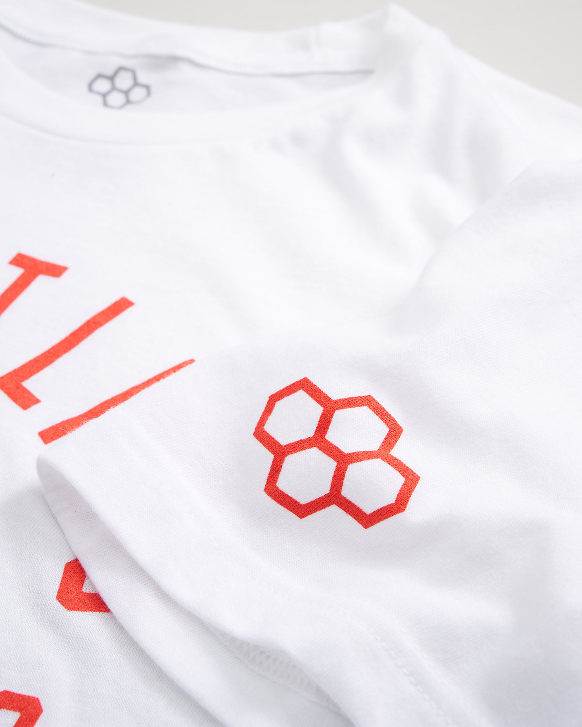 A close-up of a white t-shirt featuring bold red lettering and a geometric logo on the sleeve