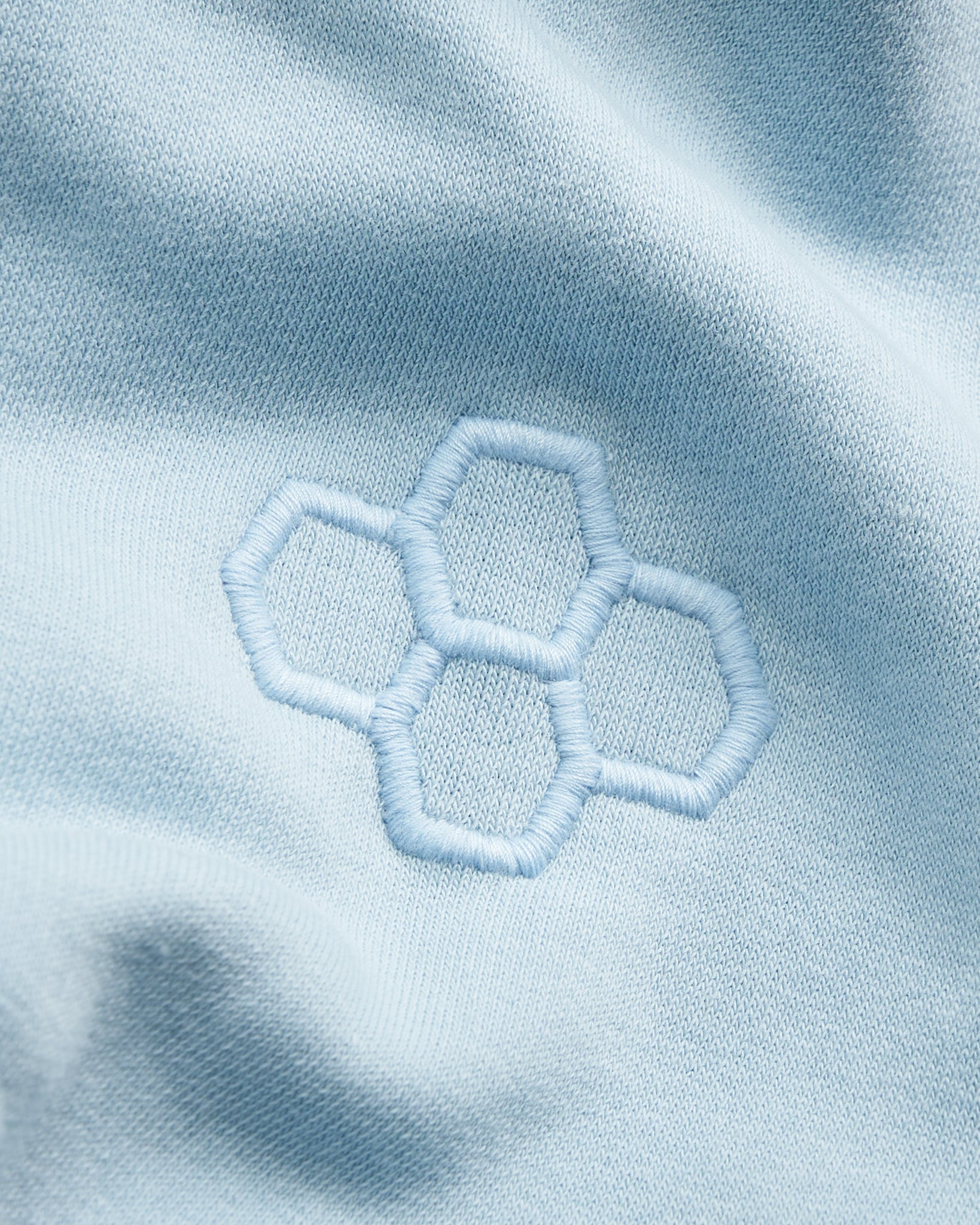 The image features a close-up of a light blue fabric with a hexagonal embroidered design highlighting texture and color
