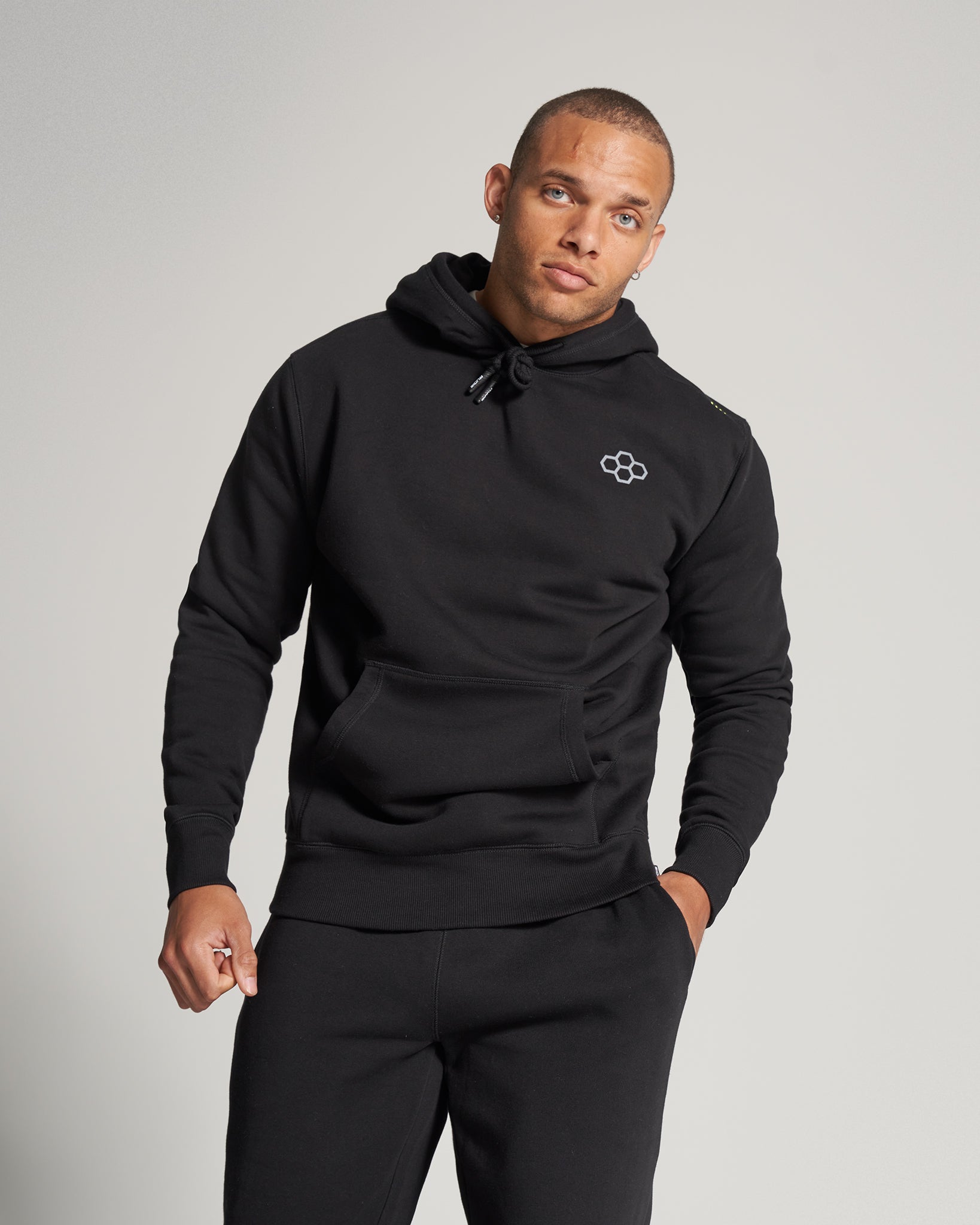 A male model wearing a black hoodie and matching sweatpants showcasing a contemporary casual style against a neutral background