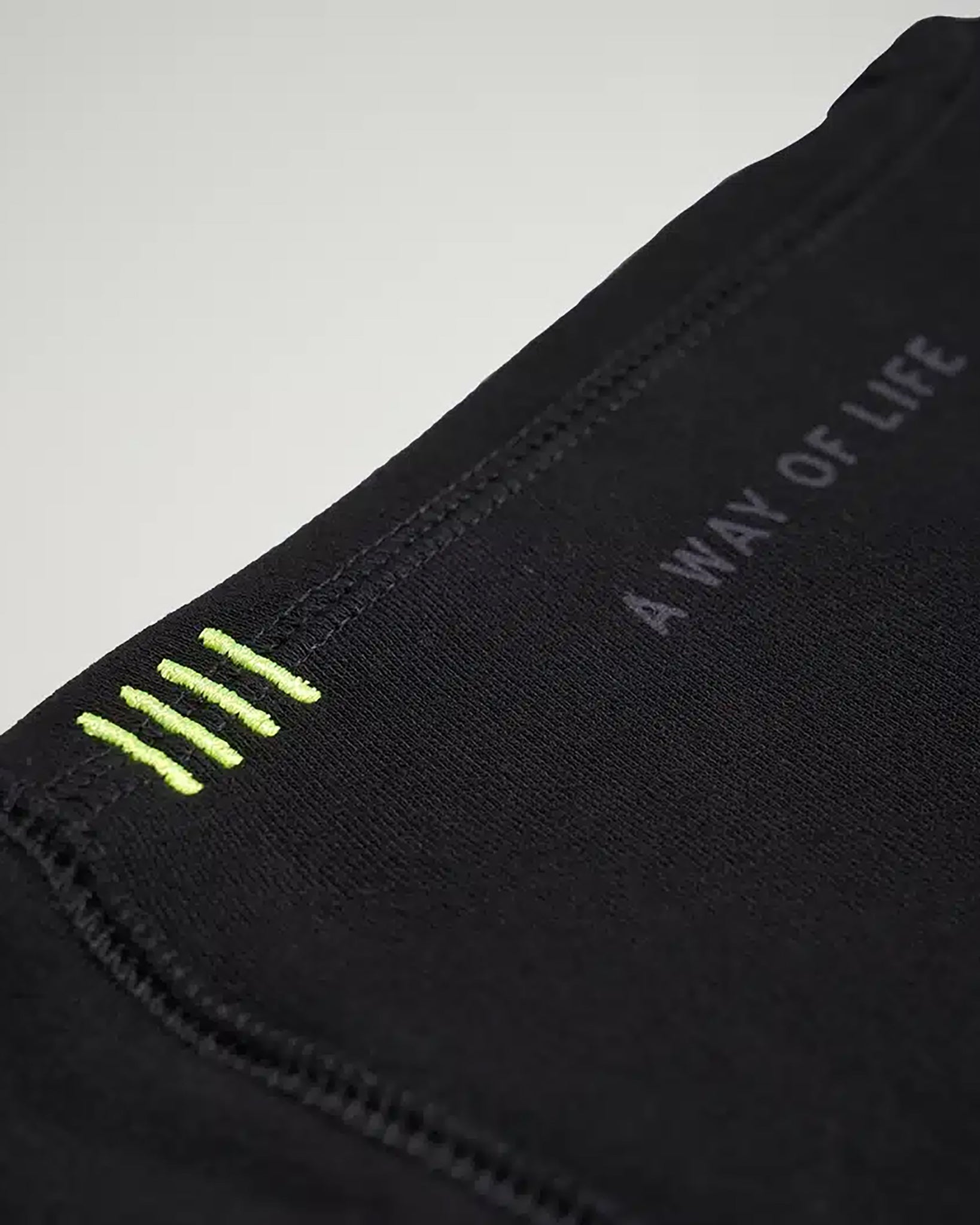 A close-up view of a black fabric featuring green stitching details and the phrase A WAY OF LIFE