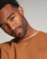 A man with a stylish look is posing in a brown sweatshirt showcasing his confident demeanor and contemporary sense of fashion