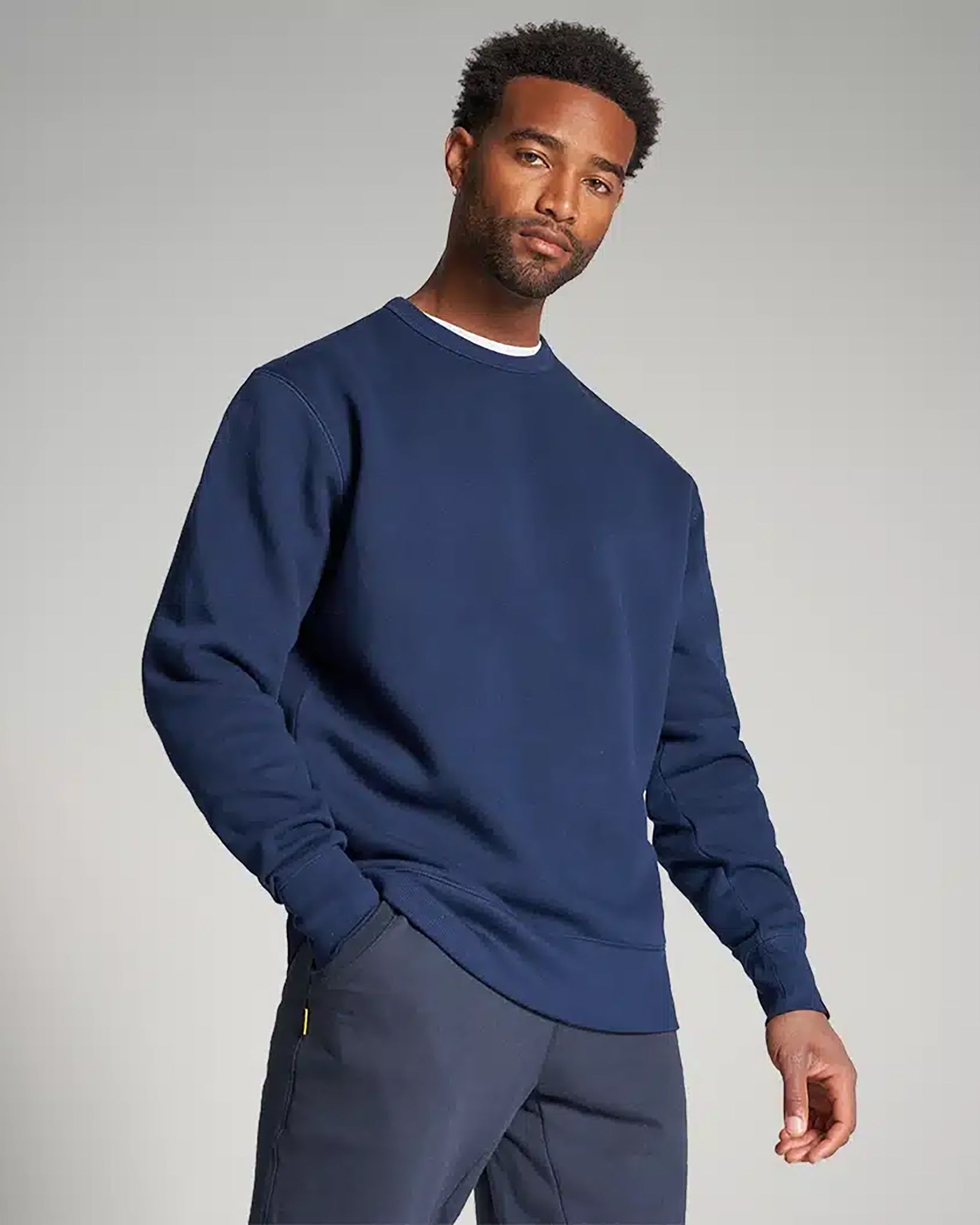 A man poses confidently in a navy blue sweatshirt paired with dark pants set against a neutral background