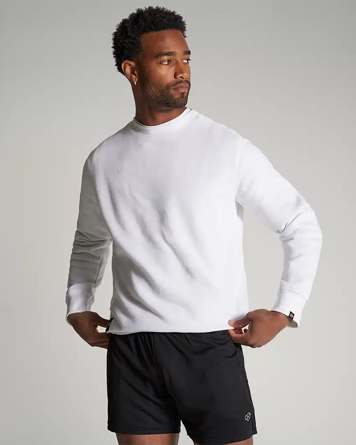 A man poses confidently in a white sweatshirt and black shorts showcasing a casual and athletic look with a neutral background