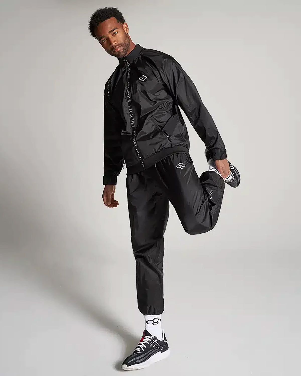 A man models a stylish black athletic tracksuit showcasing a modern design paired with signature footwear and accessories