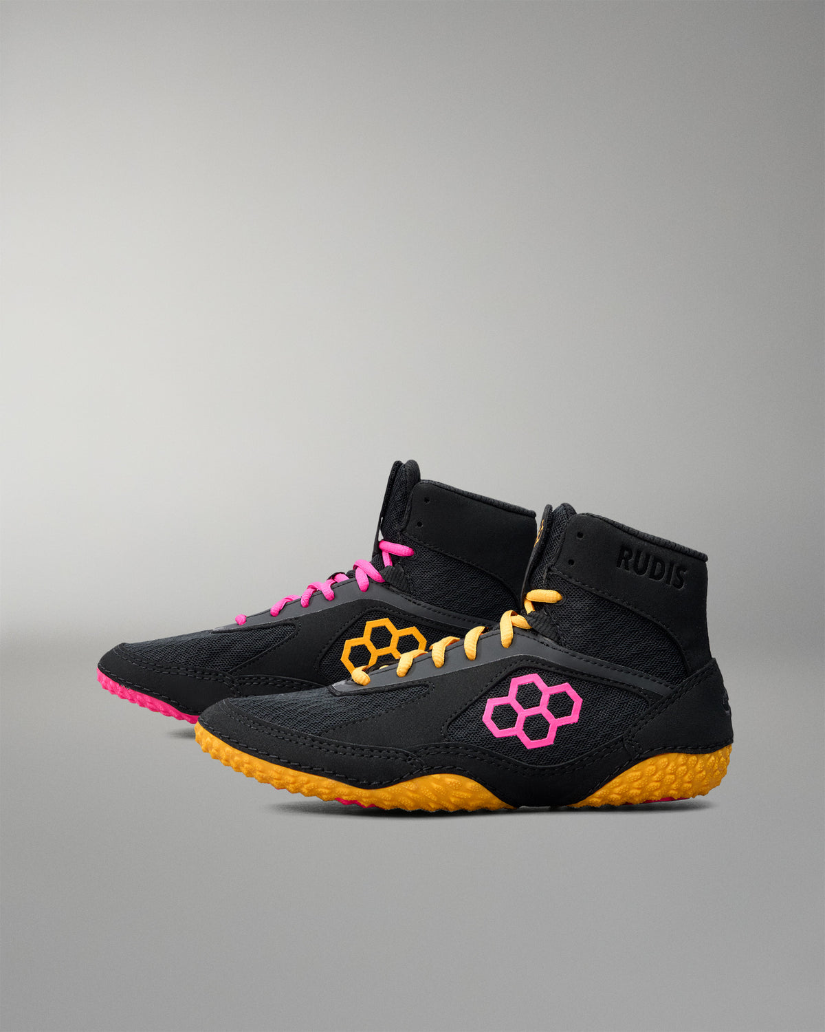 Black wrestling shoes with pink and yellow accents on a gray background