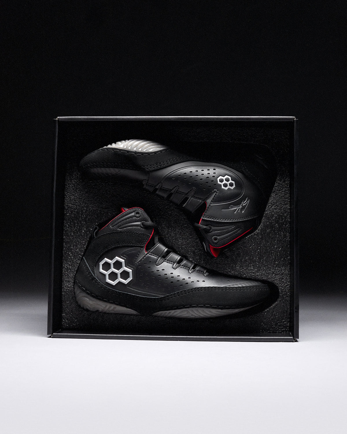 Black wrestling shoes with red accents in a black box on a dark background - Cary Kolat wrestling shoes