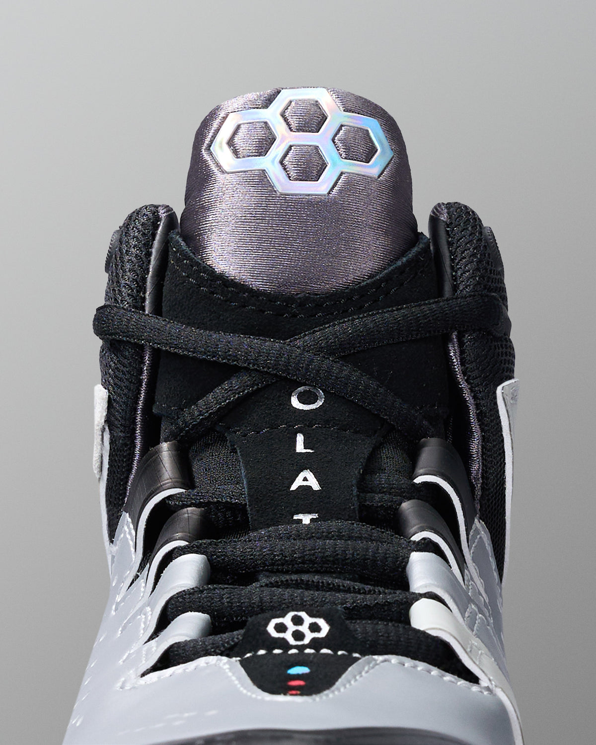 Close-up of a black and gray wrestling shoe with a hexagonal pattern on a gray background