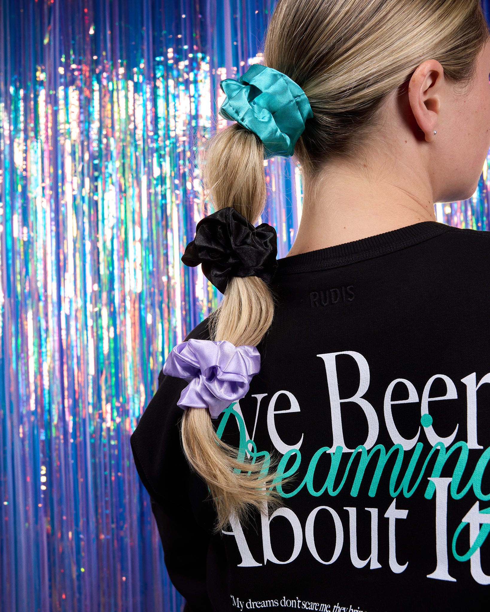 Person with scrunchies in hair against a colorful curtain background