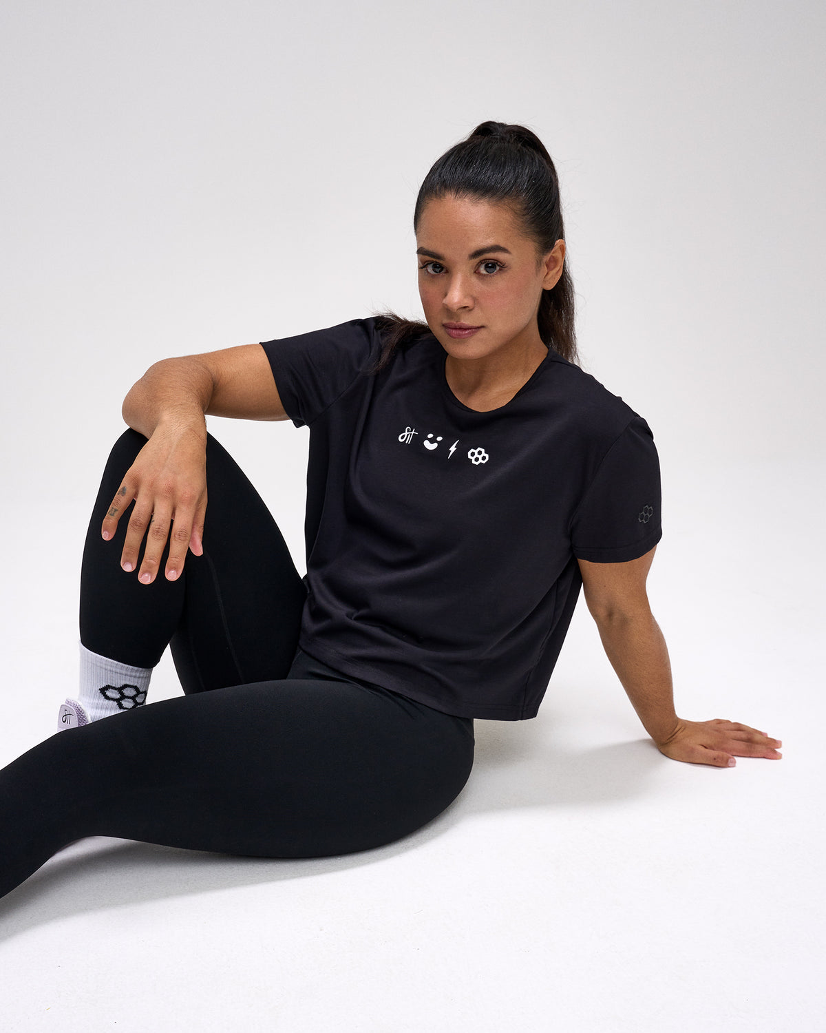 Woman wearing a black t-shirt with a logo sitting on a white background