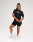 Woman modeling the black RUDIS SH Smile Elite Super Soft T-Shirt with white smile graphic, black athletic shorts, and white shoes.