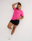 Woman modeling the pink RUDIS SH Smile Elite Super Soft T-Shirt with white smile graphic, black athletic shorts, and white shoes.