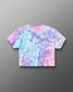 A short-sleeve crop top t-shirt with a pastel tie-dye pattern in pink, purple, and light blue, shown from the back on a gray gradient background.