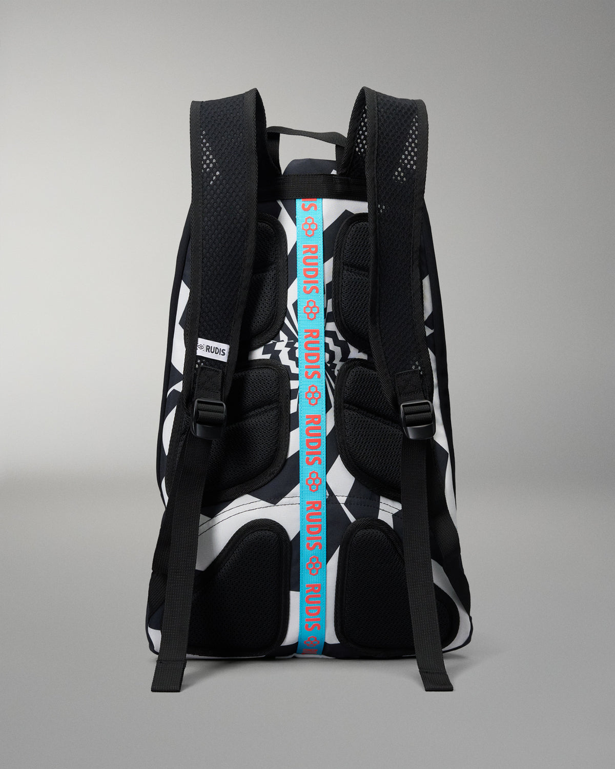 A black and white patterned backpack shown from the back, featuring a prominent vertical blue strap with white text reading 'RUDIS' and black mesh padding on the straps.