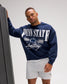 Front view of male model in the RUDIS Penn State Navy Relaxed Comfort Fleece Crewneck, showcasing Penn State Nittany Lions graphics and white Wrestling script.