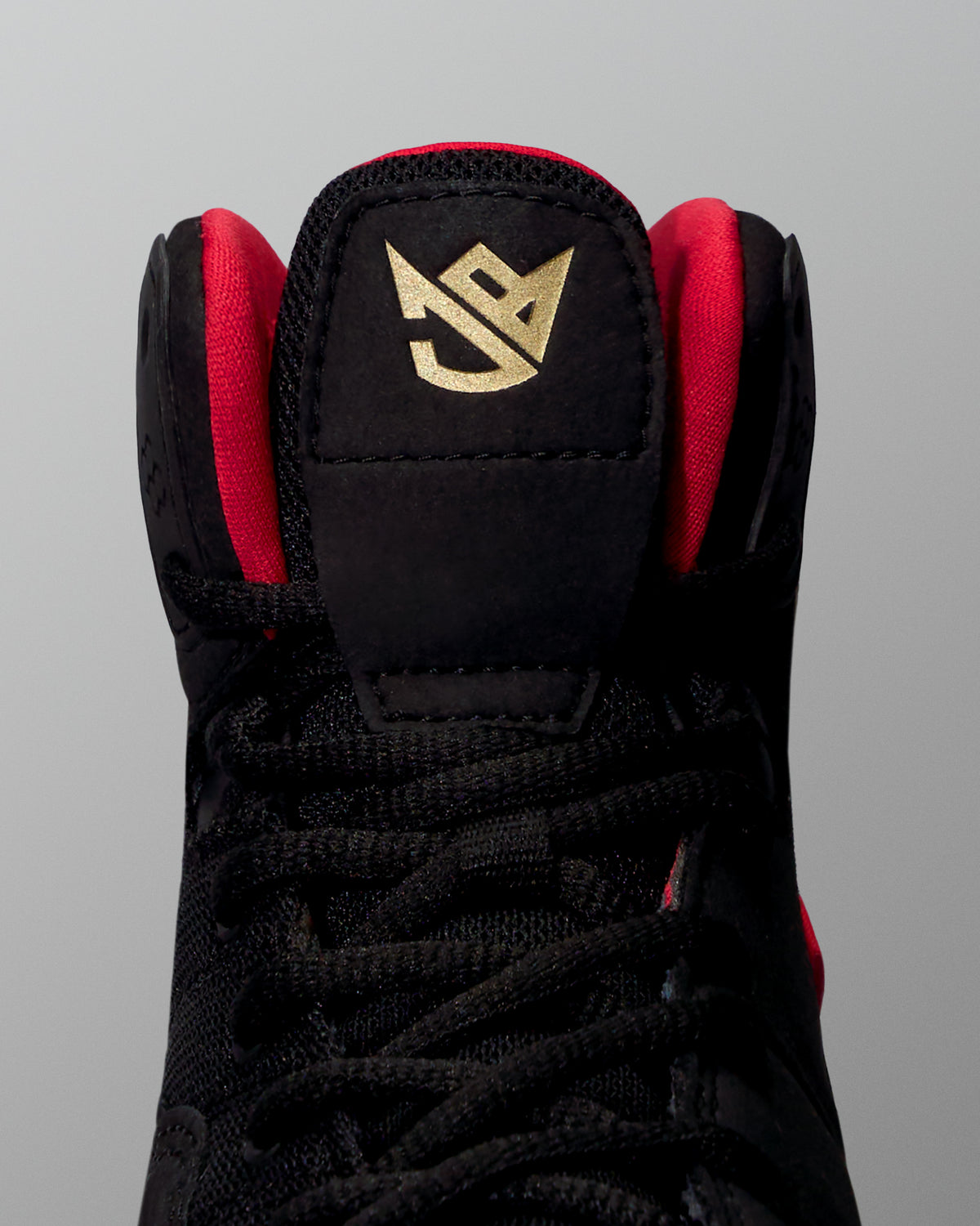 Black wrestling shoe with red accents and a gold logo on a gray background