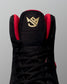 Black wrestling shoe with red accents and a gold logo on a gray background