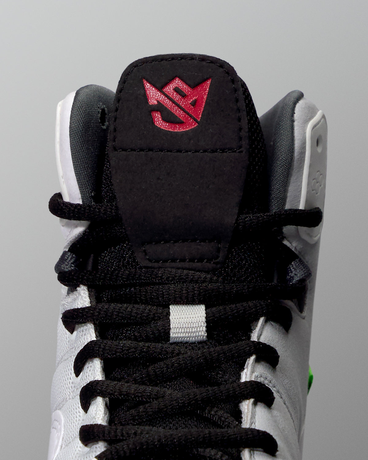 Close-up of a wrestling shoe with a black tongue and red logo on a gray background