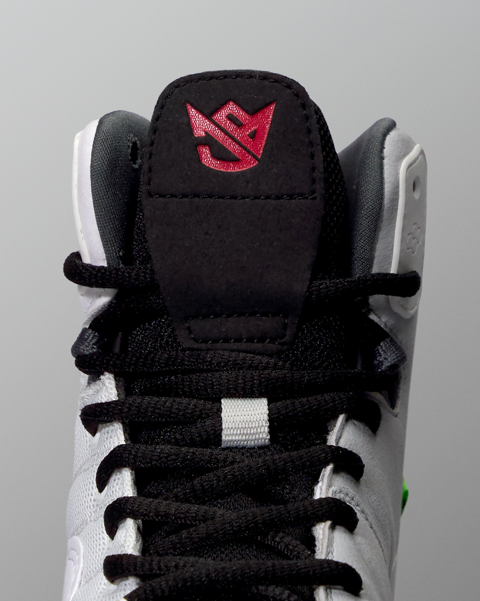 Close-up of a wrestling shoe with a black tongue and red logo on a gray background