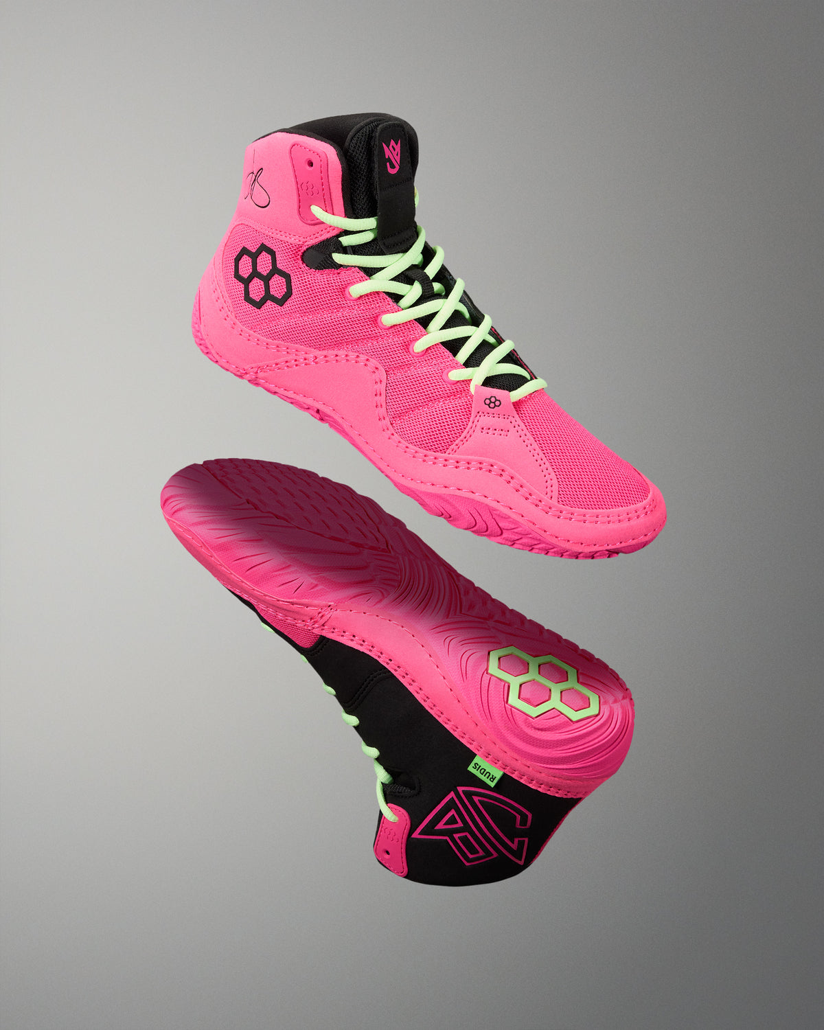 A pair of high-top athletic wrestling shoes in bright pink and black, shown floating against a neutral gray gradient background. One shoe is oriented to show the side profile with neon green laces, while the other shows the sole with a matching pink and black tread pattern.