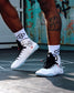 RUDIS JB1 Adult Wrestling Shoes in White Shark worn on a wrestling mat, showcasing the white high-top design, black laces, signature branding, red accents, and light blue outsole.