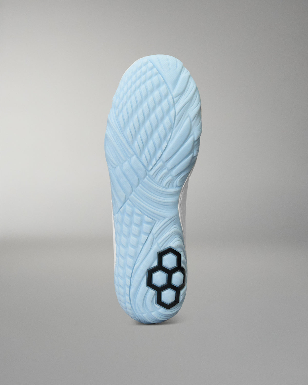 A light blue wrestling shoe sole shown from the bottom, featuring a black hexagonal logo near the heel, set against a neutral gray background.
