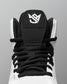 Close-up of a high-top wrestling shoes showing the black tongue patch with a white stylized logo, black laces, and white upper against a gray background.