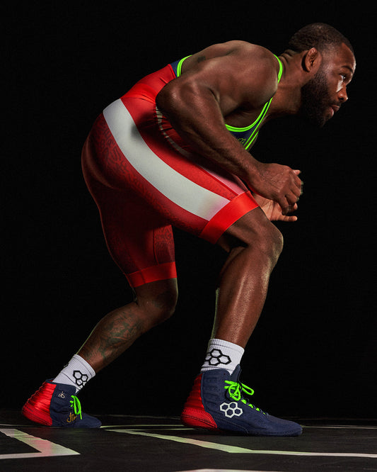 Athlete in red wrestling singlet and blue shoes with green accents on a black background