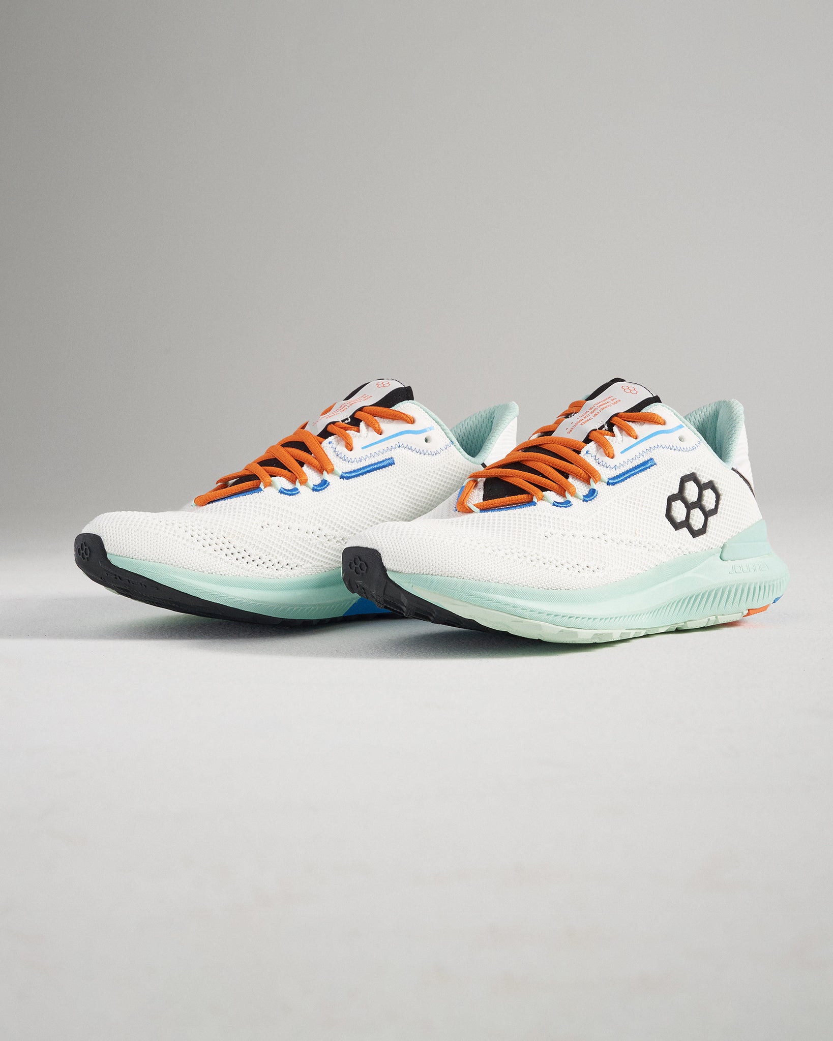 A modern pair of white athletic shoes with vibrant orange laces and a unique design featuring a hexagonal logo on the side