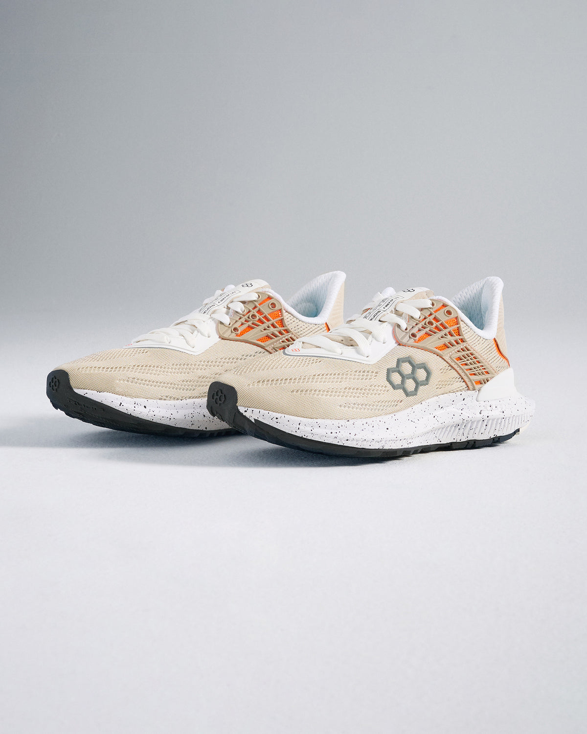 A pair of light beige running shoes featuring an airy mesh upper and contrasting orange details designed for comfort and performance