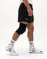 A person wearing black athletic shorts with a small white script logo, a black knee sleeve, white crew socks with a black floral pattern, and white high-top sneakers, shown against a plain light gray studio background.