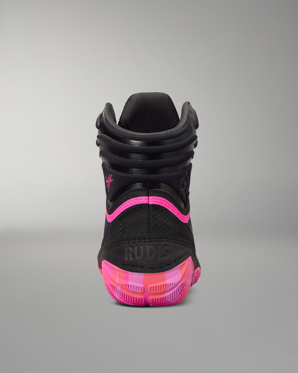 A high-top black wrestling shoe shown from the rear, featuring a black textured upper, a vibrant hot pink curved accent line, and a translucent pink and orange sole with the brand name 'RUDIS' embossed on the heel.
