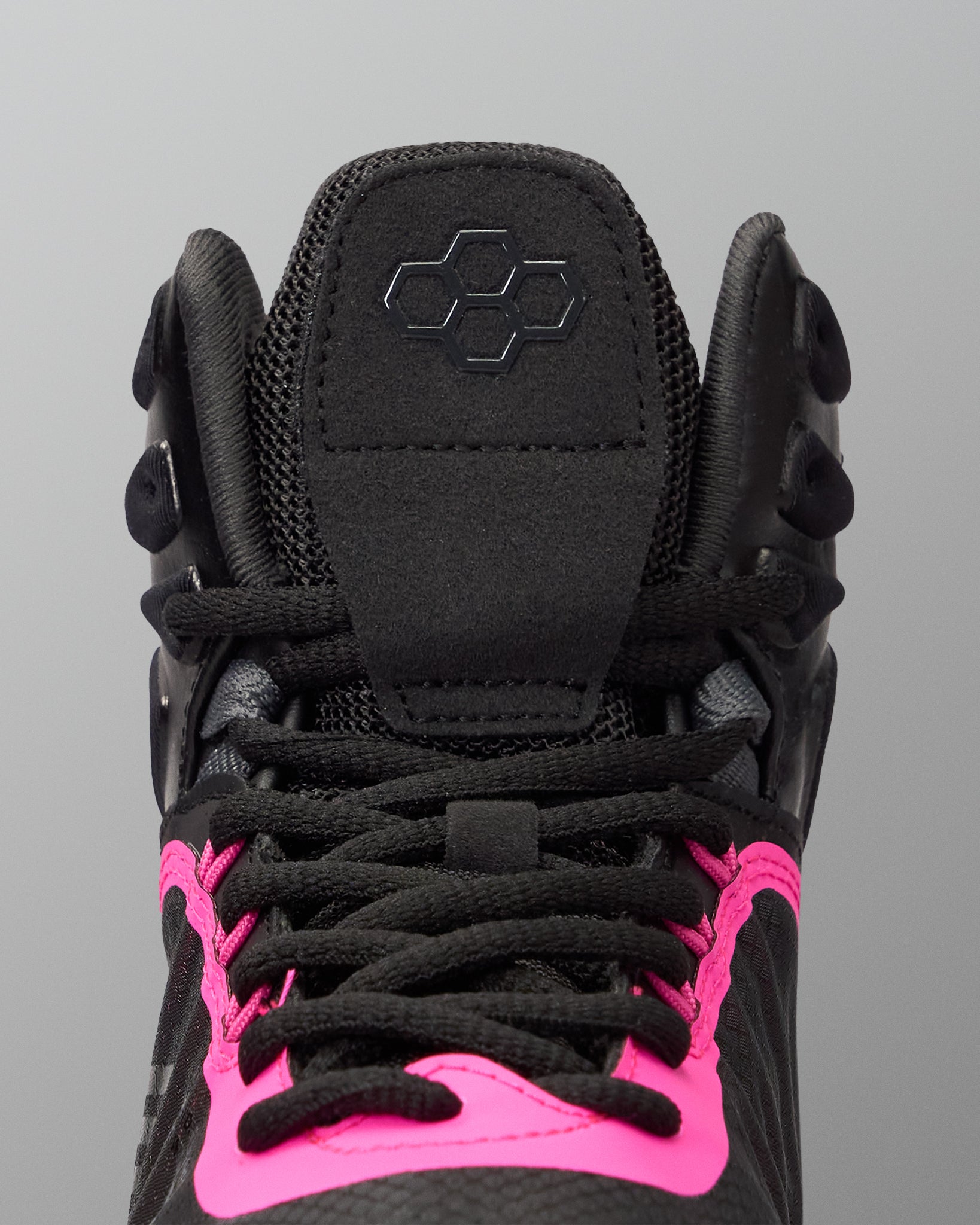 Close-up of a high-top black wrestling shoe with bright pink accents around the laces and tongue, featuring a black geometric logo on the tongue.