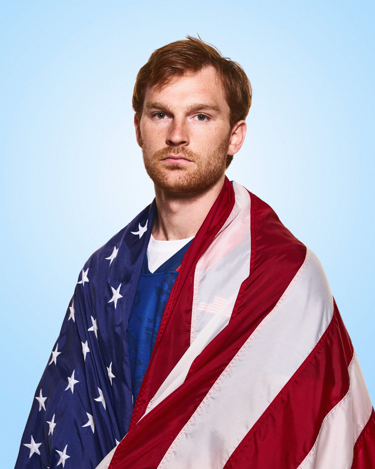 Pat Kavanagh, RUDIS lacrosse athlete, featured in a portrait wearing an American flag over his lacrosse uniform, representing elite competition and performance.