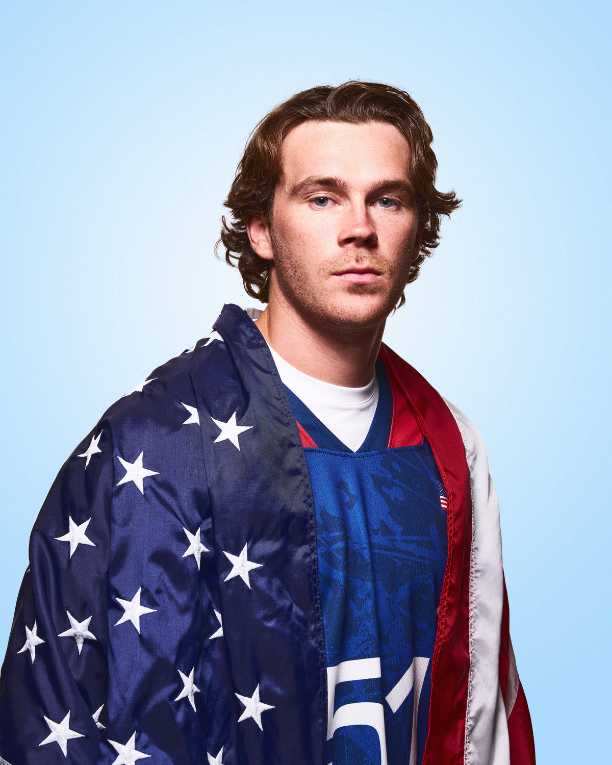 Pat Kavanagh, RUDIS lacrosse athlete, wearing an American flag over his lacrosse uniform in a portrait celebrating elite competition and the pursuit of excellence.