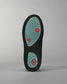 A detailed view of a black shoe sole featuring a patterned grip made from a mint green material and red accents
