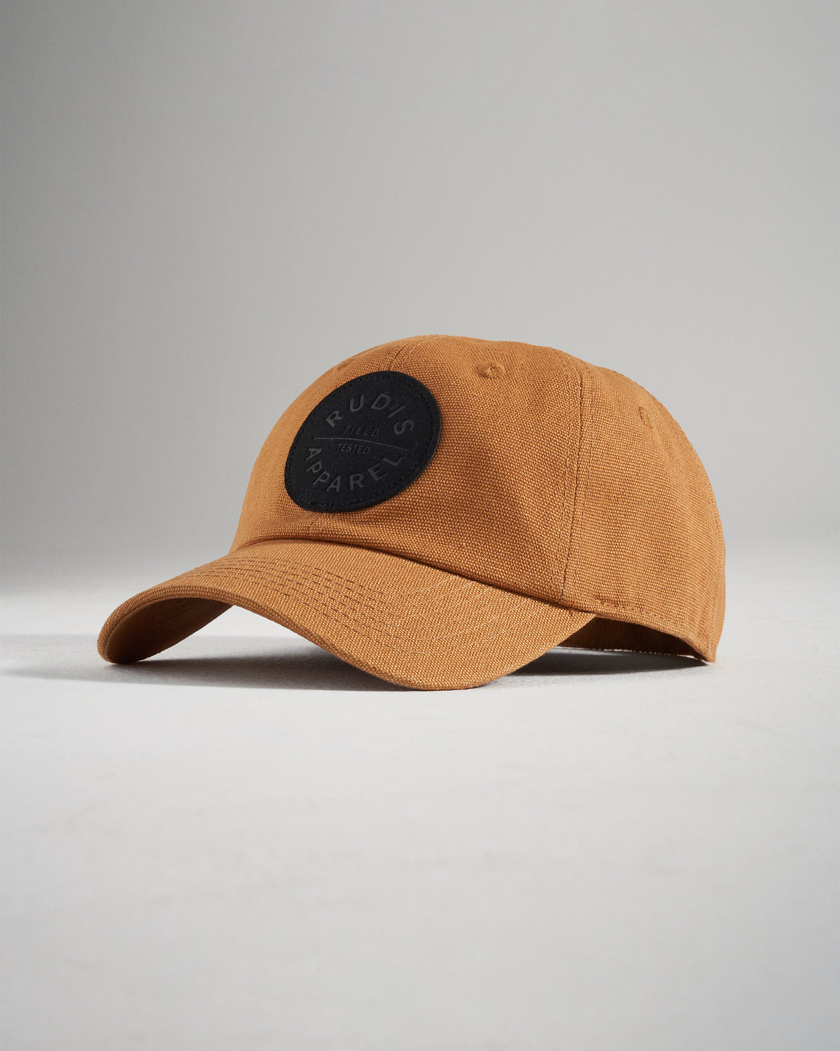 A stylish brown cap featuring a black circular logo with the text RUDIS APPAREL