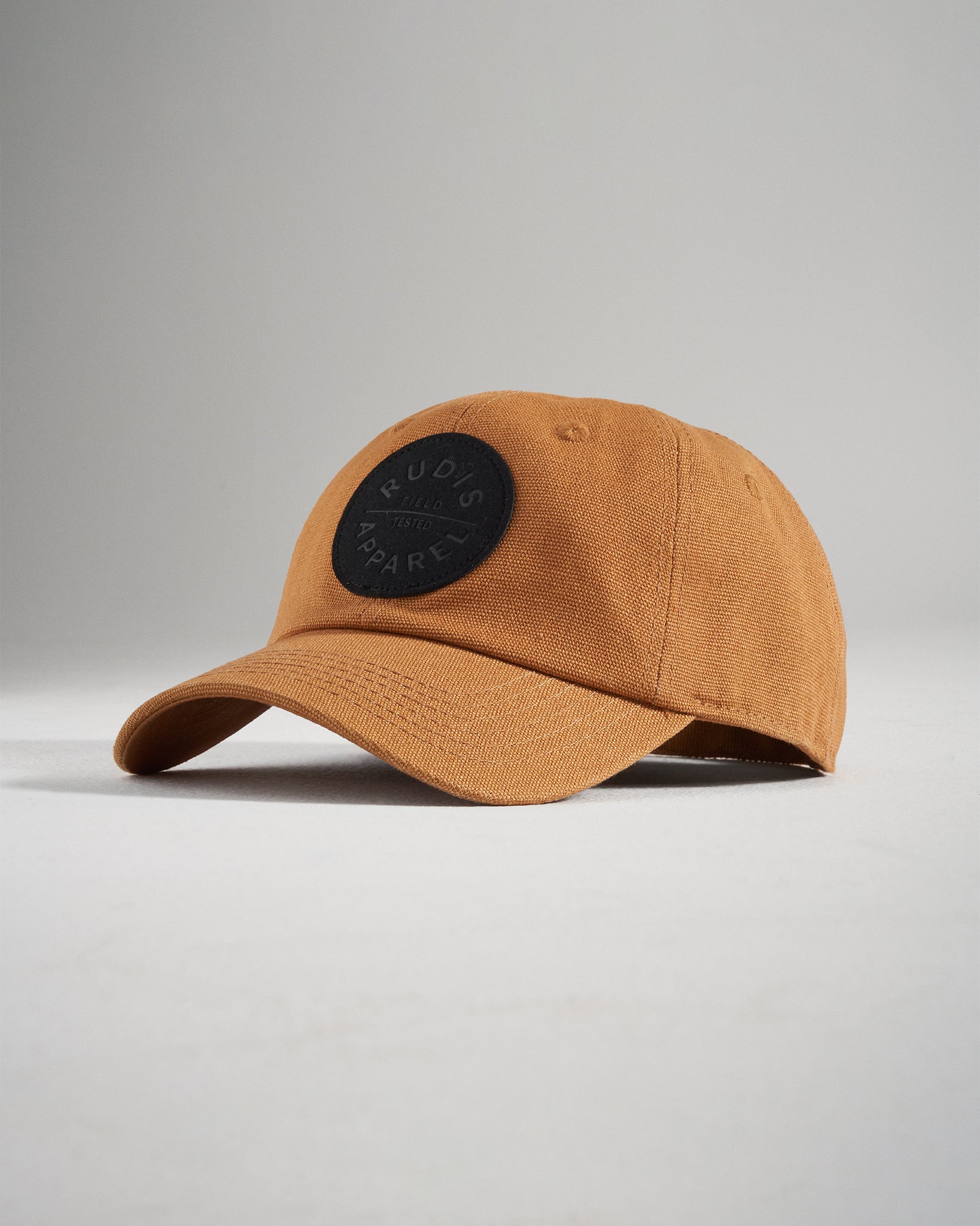A stylish brown cap featuring a black circular logo with the text RUDIS APPAREL