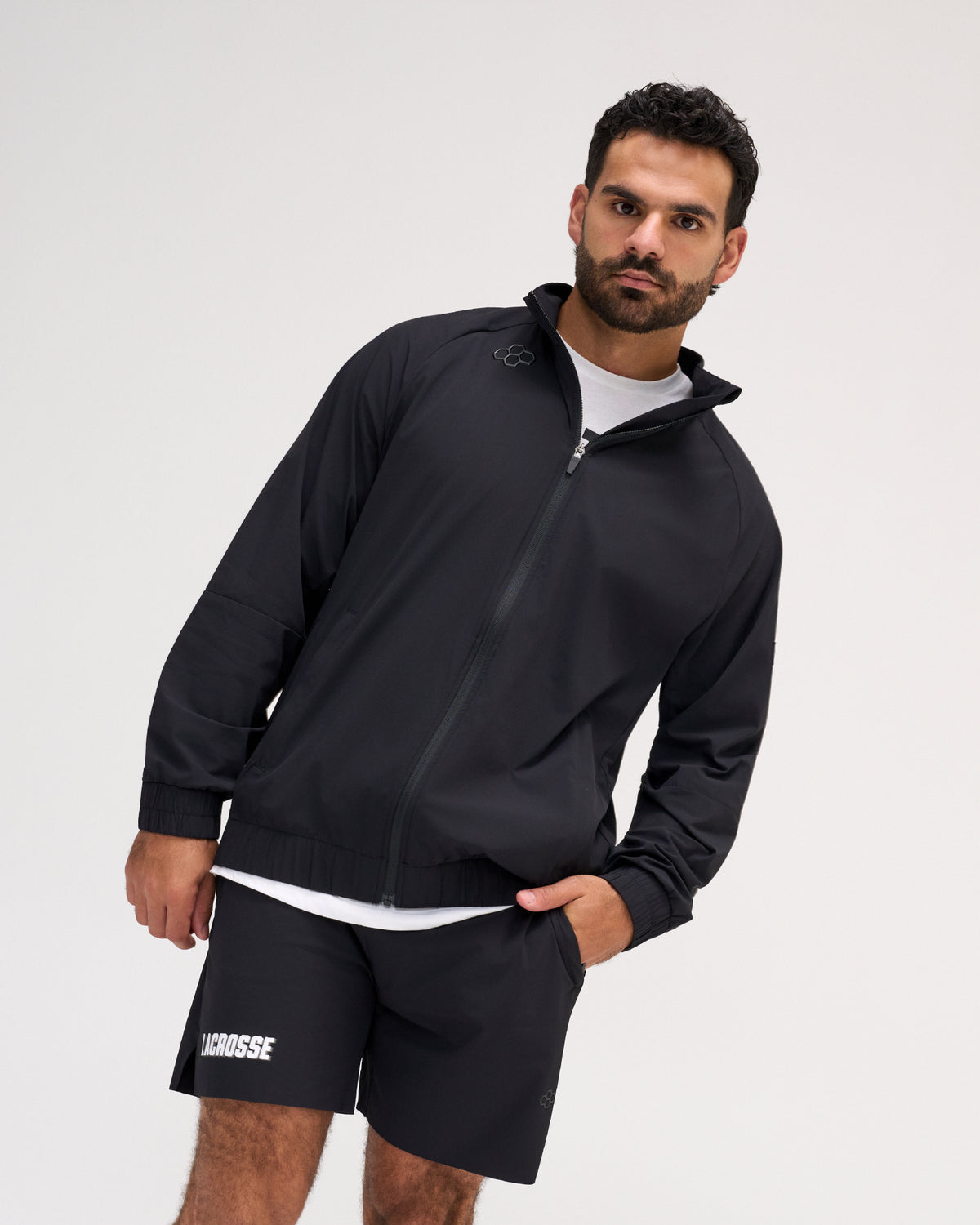 A man wearing a black full-zip jacket and matching black shorts with white Lacrosse branding, posed against a light gray studio background.
