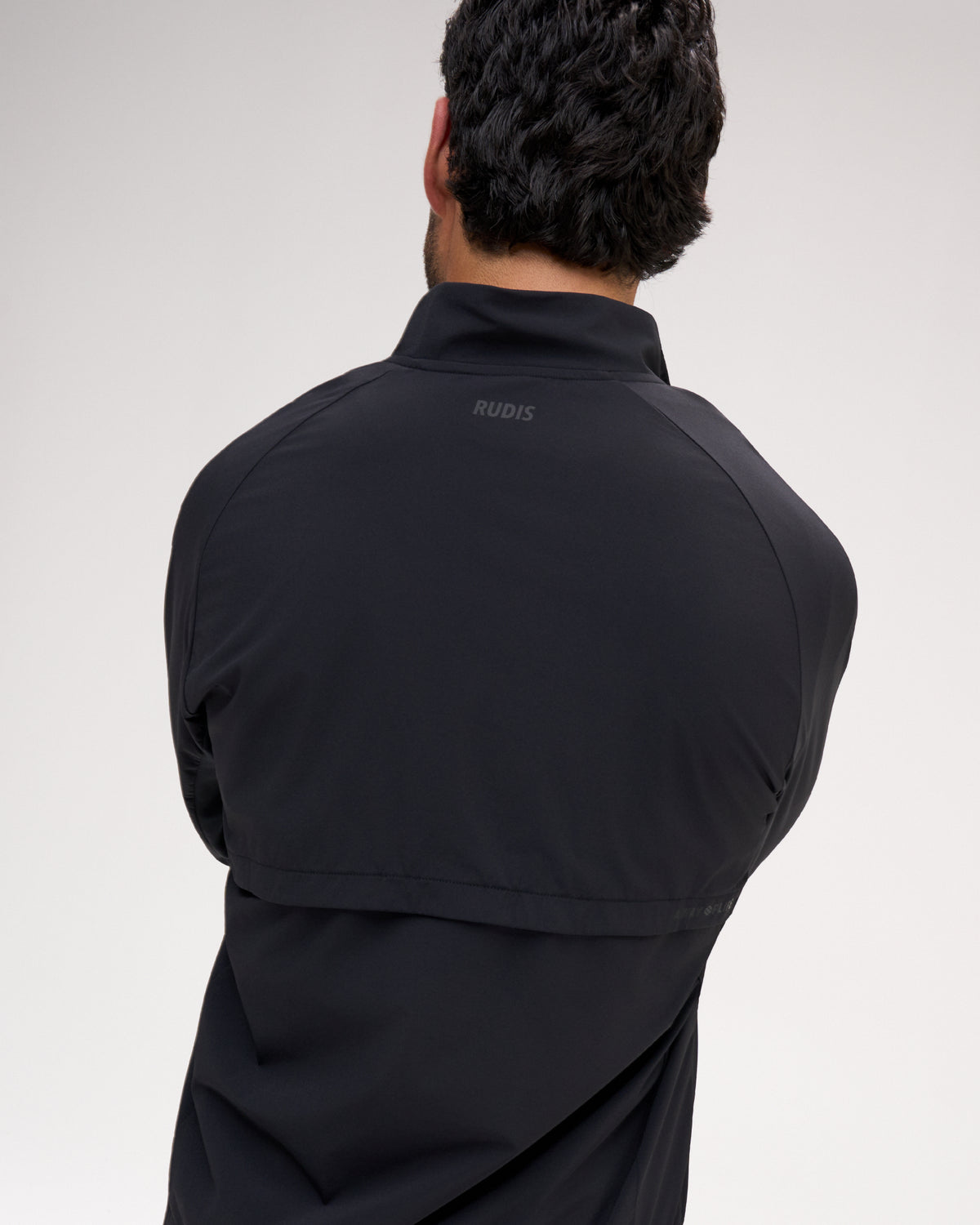 Rudis black athletic quarter-zip jacket shown from the back on a model, featuring a subtle gray brand logo on the upper neck.