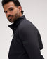 A man wearing a black zip-up athletic jacket, shown in a close-up side profile against a light gray studio background. A rectangular brand patch is visible on the upper sleeve.